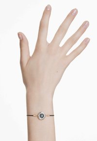 Svart snoddarmband med en cirkulär silver- och blå emaljberlock, som har intrikata detaljer och en slät yta.