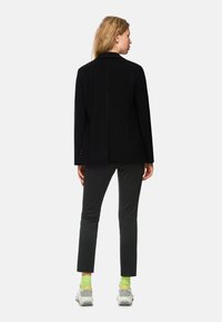 Black blazer with a tailored fit, long sleeves, and a smooth texture. Paired with dark grey pants and grey sneakers with neon green accents.