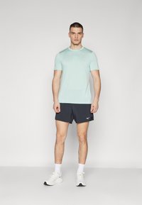 Camiseta atlética de manga corta en turquesa claro combinada con pantalones cortos azul marino. El conjunto presenta un diseño minimalista e incluye zapatillas deportivas blancas.