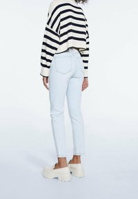 Paski, krótki sweter w kolorze kremowo-granatowym, jasnoniebieskie obcisłe dżinsy i masywne białe buty na platformie. Posiada żebrowane mankiety i tylne kieszenie.