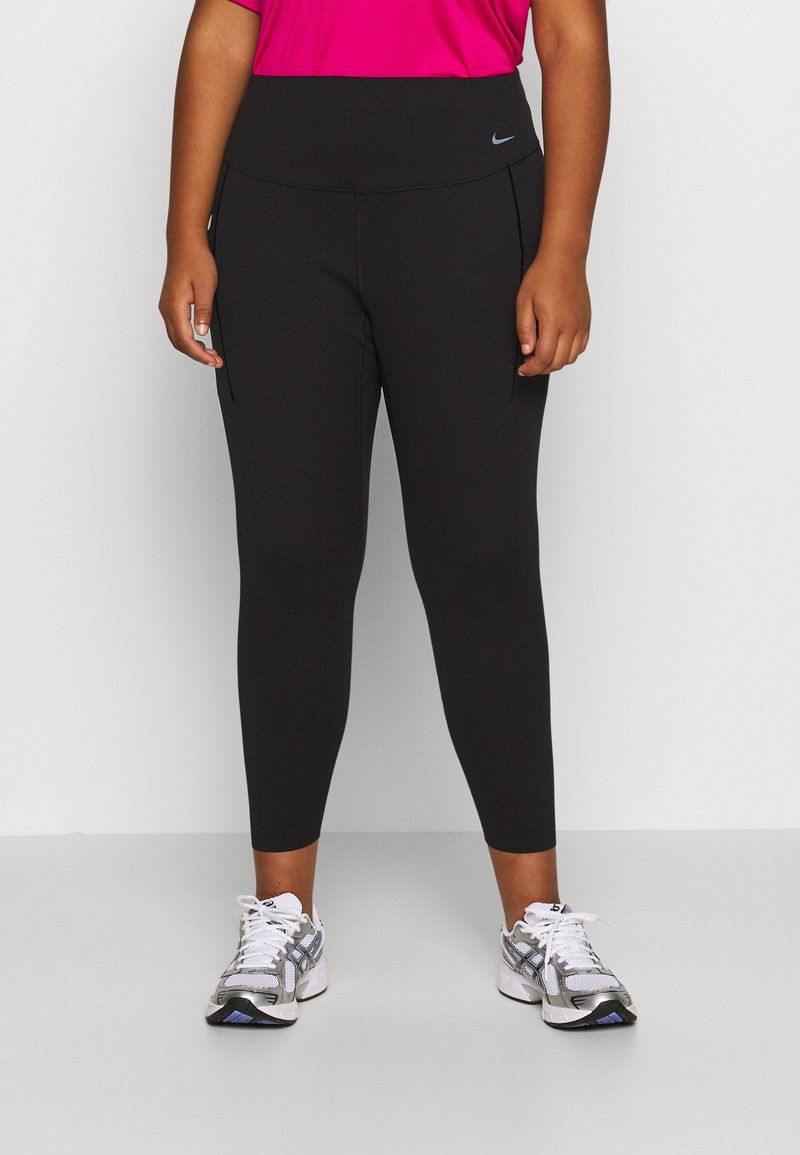 Sorte leggings med høj talje, der har et lille blåt logo på fronten, parret med grå træningssko. Glat tekstur, tætsiddende design.