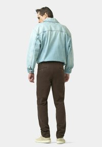 Veste en denim bleu clair avec des coutures visibles, associée à un pantalon marron. L'ensemble comprend des baskets de couleur crème et une coupe décontractée.