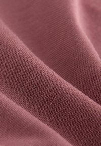 Gros plan sur un tissu rose poussiéreux montrant une fine texture en maille côtelée et de doux plis.