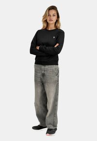 Black sweatshirt with crew neckline, ribbed cuffs, and hem; embroidered logo. Paired with light gray baggy jeans and black sneakers.