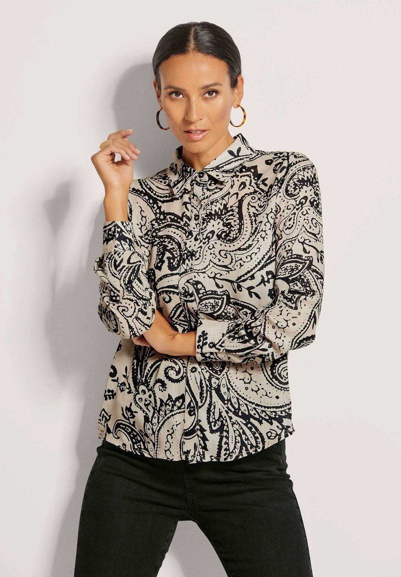 Bluse in Schwarz und Creme mit Paisleymuster, Kragen, langen Ärmeln und Knopfverschluss, aus leichtem Stoff gefertigt.