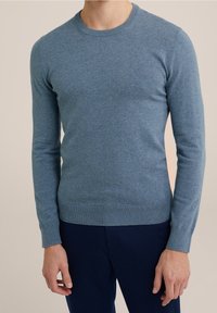 Blauer Strickpullover mit Rundhalsausschnitt, langen Ärmeln und gerippten Bündchen. Leichter Stoff mit weicher Textur. Kombiniert mit dunklen Hosen.