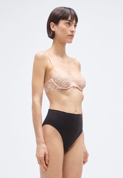 Csipke melltartó testszínben, virágmintás hímzéssel, magas derekú fekete alsóval párosítva, áttetsző és sima textúrákat bemutatva.