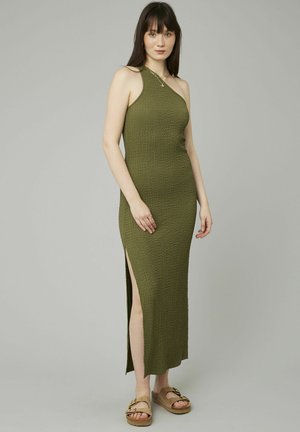 Robe maxi en tricot vert avec design à une épaule, fente sur le côté, tissu texturé, associée à des sandales à plateforme marron.
