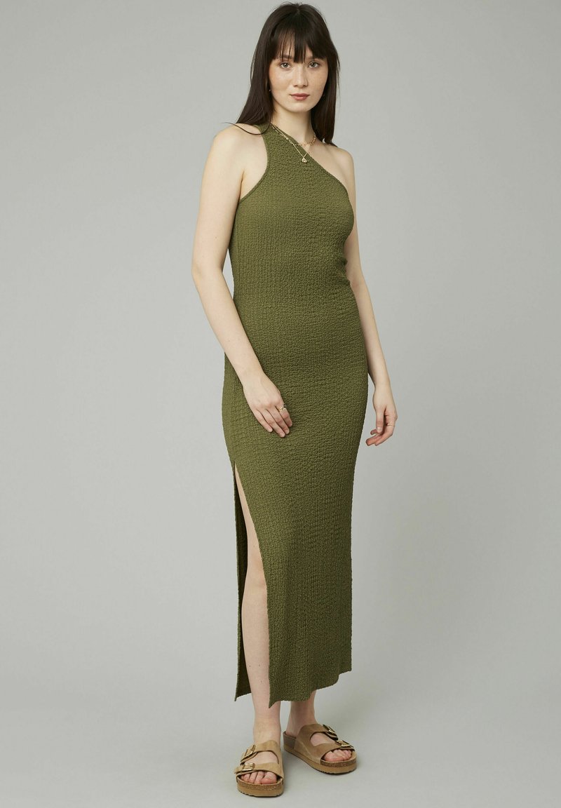 Robe maxi en tricot vert avec design à une épaule, fente sur le côté, tissu texturé, associée à des sandales à plateforme marron.