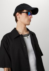 Black button-up short-sleeve shirt, white ribbed tank top underneath, black baseball cap, and reflective sunglasses with colorful lenses.