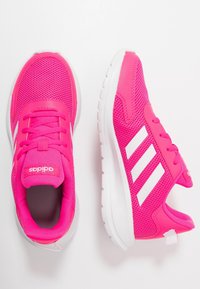 Zapatillas de correr Adidas de color rosa brillante con franjas y suelas blancas, mostradas en vista lateral y superior sobre un fondo blanco.