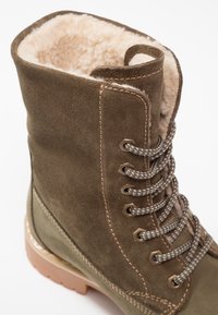 Botte en daim marron avec doublure en fourrure beige. Comprend une cheville renforcée, des œillets métalliques et des lacets texturés ; semelle en caoutchouc avec des accents marron clair.