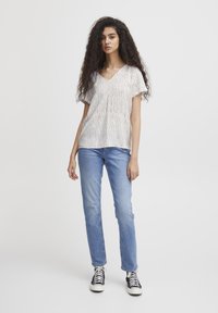 Top a maniche corte con scollatura a V, caratterizzato da un motivo a righe testurizzato in bianco, rosso e verde. Abbinato a jeans in denim azzurro chiaro e sneakers nere.