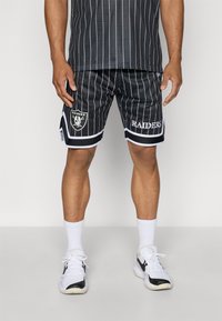 Black mesh sports shorts feature vertical white stripes, a Raiders logo on the left leg, and white trim at the hem. Paired with white socks and sneakers.