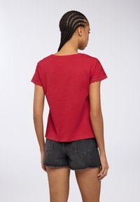 T-shirt rossa in cotone con dettagli in pizzo sulle maniche corte, taglio leggermente oversize e scollatura rotonda. Abbinato a pantaloni corti di jeans neri.