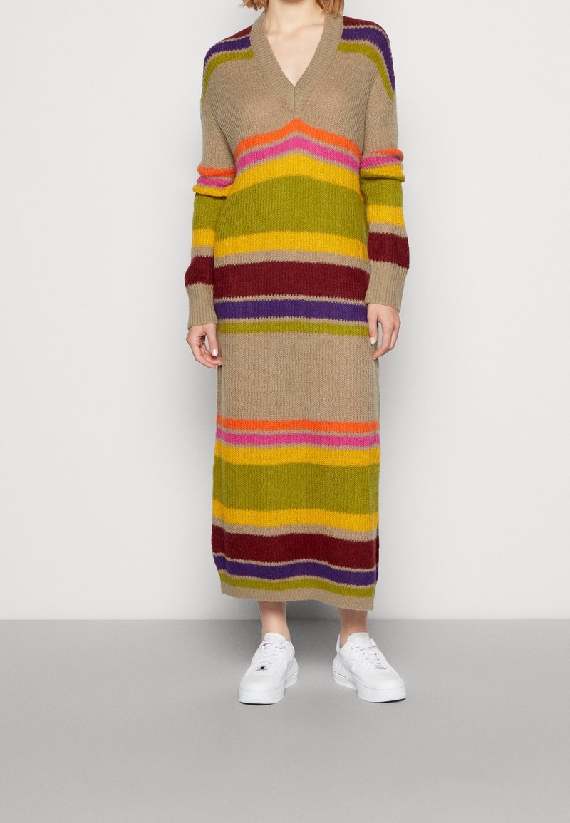 Robe tricotée longue à rayures marron, vert, jaune, violet, rose et orange avec un col en V et des manches longues. Associée à des baskets blanches.
