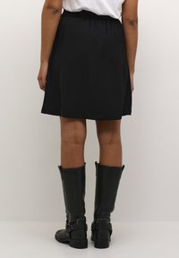 Jupe noire en A avec une taille élastique, longueur genou, assortie à des bottes en cuir noires jusqu'au genou avec des détails de boucle.