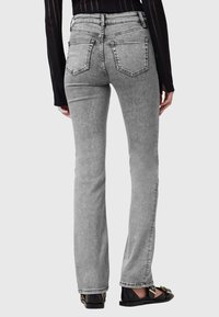 Jeans a zampa d'elefante in denim grigio con una texture liscia, design a cinque tasche, dettagli cuciti e vita alta, abbinati a sandali neri flat.