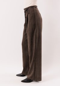 Pantaloni marroni a gamba larga in tessuto strutturato, con coulisse nera in vita e pieghe sottili per un dettaglio raffinato.