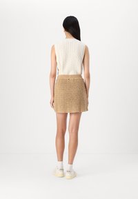 Strikket kremfarget ermeløs topp med kabeltekstur, kombinert med et beige heklet mini-skjørt. Casual hvite sneakers fullfører stilen.