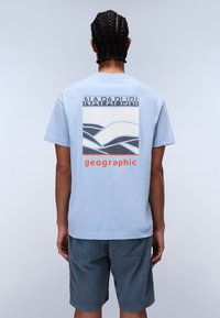 Light blue cotton t-shirt with a graphic design featuring waves and the text "NAPAPIJRI geographic" in orange. Short sleeves and relaxed fit.
