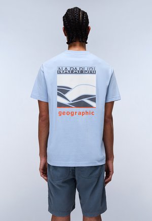 T-shirt di cotone blu chiaro con una grafica che presenta onde e il testo "NAPAPIJRI geographic" in arancione. Maniche corte e vestibilità comoda.