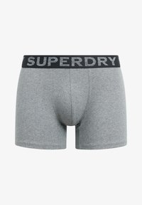 Los bóxers de algodón gris presentan un ajuste ceñido con una cinturilla elástica negra que muestra el nombre de la marca "SUPERDRY" en letras plateadas.