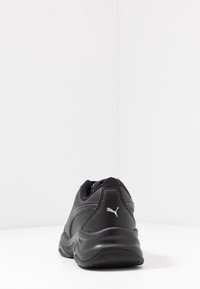 Scarpe da ginnastica nere con tomaia in pelle sintetica, design arrotondato, collare imbottito e logo Puma bianco sul tallone. Suola testurizzata.