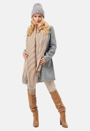 Grauem Mantel über einem hellen Oberteil, beige-gelb gestreifter Schal mit Fransen, graue Strickmütze, braune kniehohe Stiefel, glatte Textur.