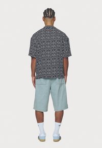 Camisa de manga curta em padrão preto e branco, com um ajuste confortável, combinada com calções de ganga azul claros. Apresenta bolsos nas costas e um design casual.