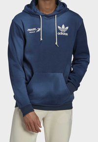 Námořnická modrá mikina s kapucí vyrobená z měkké tkaniny, s přední kapsou, bílými šňůrkami a logem Adidas trefoil na hrudi.