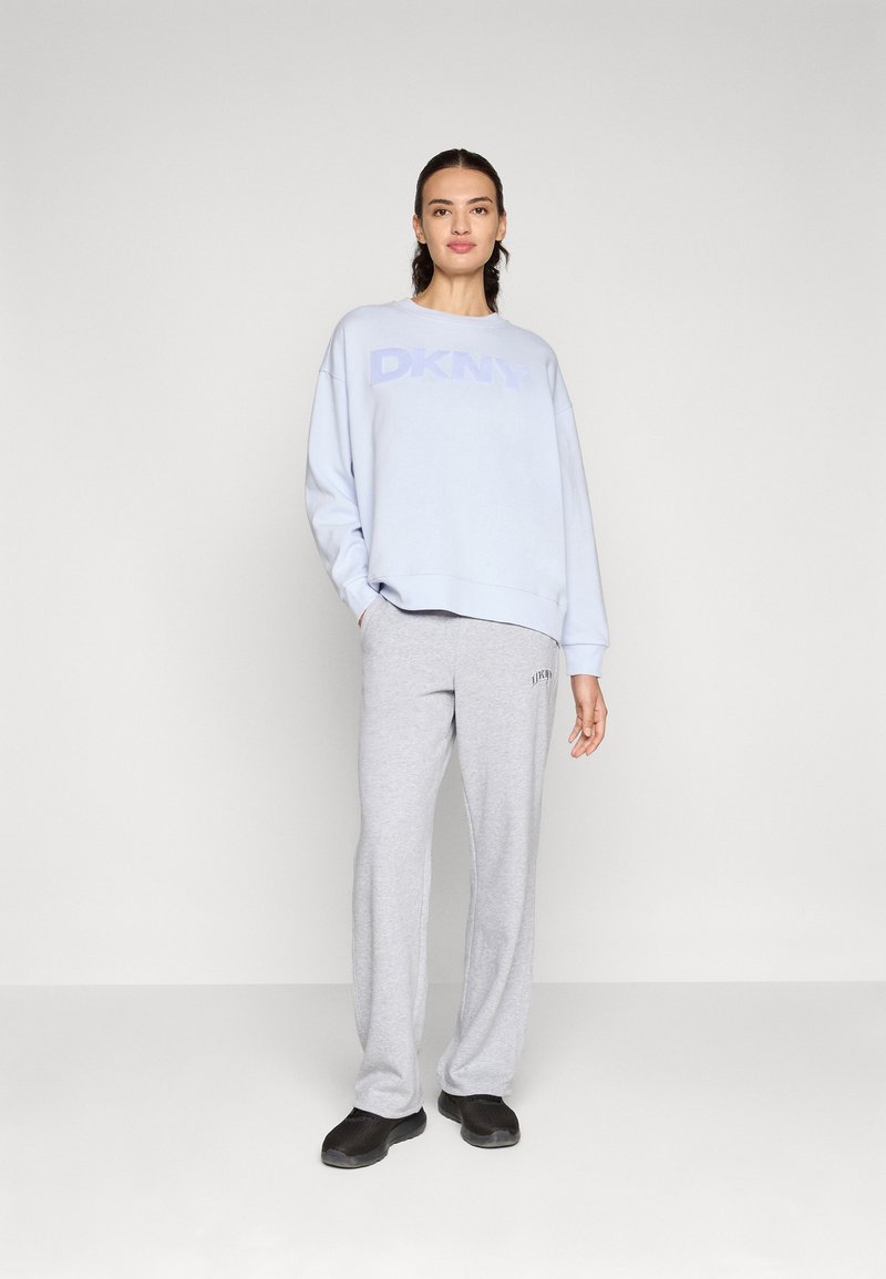 Jasnoniebieska bluza z kapturem z logo DKNY, w połączeniu z szarymi Spodniami dresowymi z detalem z logo oraz czarnymi butami. Gładki materiał, luźny krój.