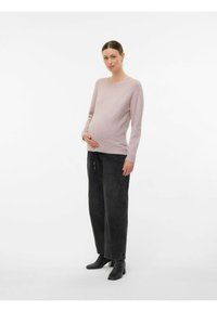 Ljusrosa långärmad stickad tröja, mjukt material; kombinerad med lösa svarta denimbyxor och svarta klackstövlar. Modellen håller om magen i stående pose.