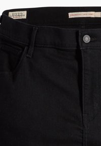 Jeans ajustados negros hechos de mezclilla, con una cintura alta, diseño de cinco bolsillos, cierre de botón de metal y detalles de costura sutiles.