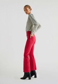 Røde flagrende jeans med fem lommer og høj talje, parret med en lysegrå striktrøje og sorte ankelstøvler.