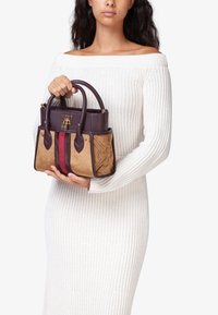 Borsa viola e beige con dettagli floreali, hardware dorato, doppi manici superiori e strisce verticali in rosso e marrone scuro. Suede e pelle texture.