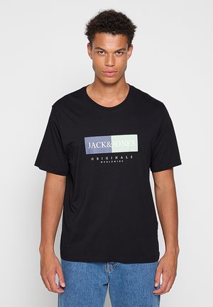 Jeune homme portant un t-shirt noir Jack & Jones Originals Worldwide et un jean bleu, faisant face à l'avant avec une expression neutre.