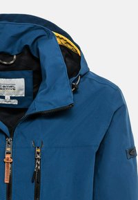 Blaue wasserdichte Jacke mit einer gelben gefütterten Kapuze, Reißverschlusstaschen vorne und braunem Lederaussehen. Sie zeichnet sich durch strapazierfähigen Stoff und ein verstellbares Design aus.