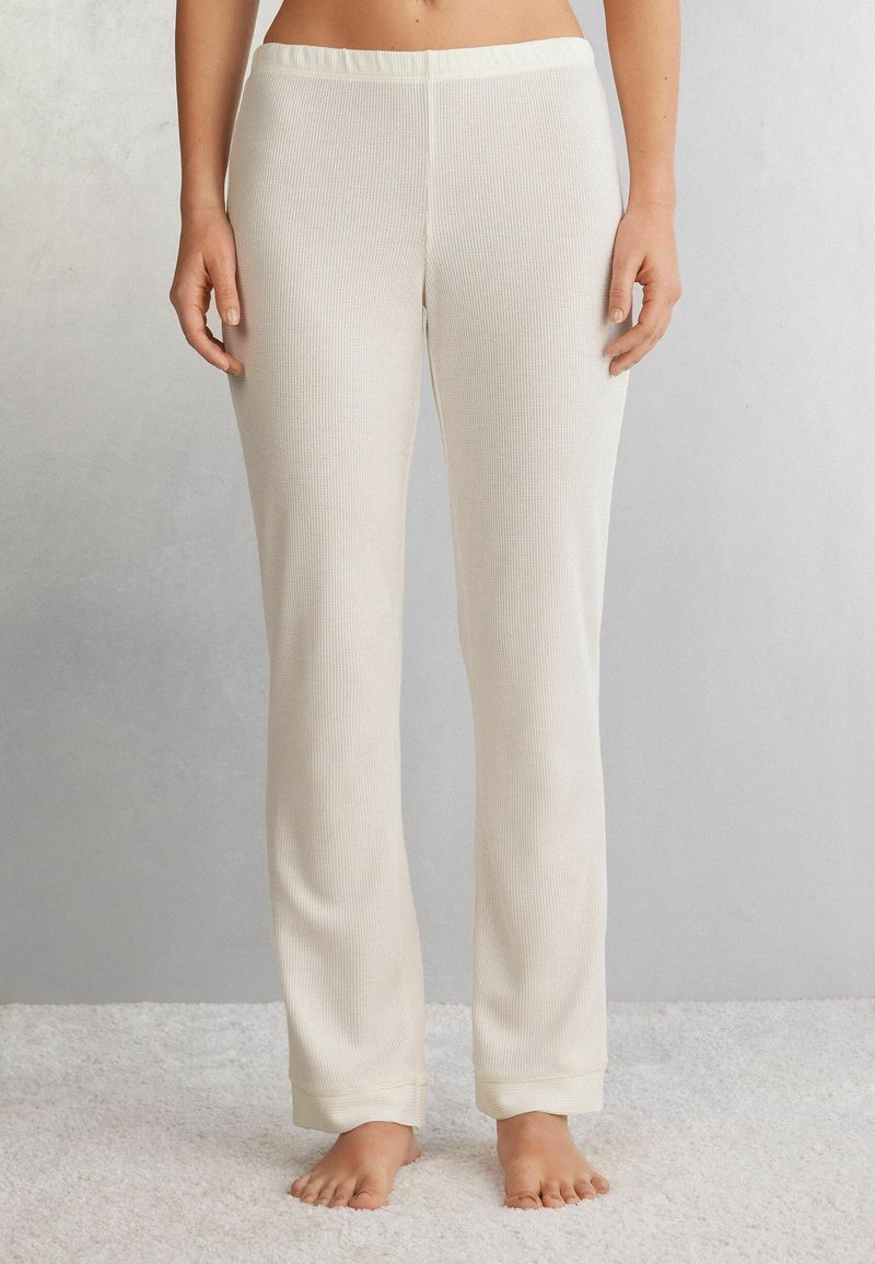 Witte geribde pyjamabroek met een brede elastische tailleband, rechte pijpen en strakke boorden bij de enkels, weergegeven op een lichte achtergrond.