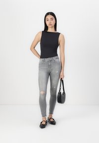Bodysuit noir sans manches, jean skinny gris clair avec des déchirures au niveau des genoux, ballerines noires à clous et un petit sac à main noir texturé.