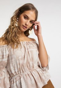 Blusa senza spalle in beige chiaro con motivi floreali e paisley bianchi, caratterizzata da una vita elasticizzata e maniche ampie.