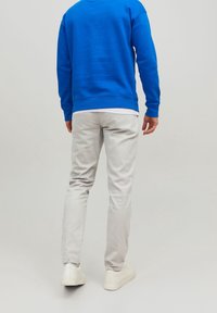 Pantaloni slim-fit grigi chiari abbinati a un felpa blu; presenta un collo rotondo e polsini a costine. Design semplice, materiale in cotone morbido.