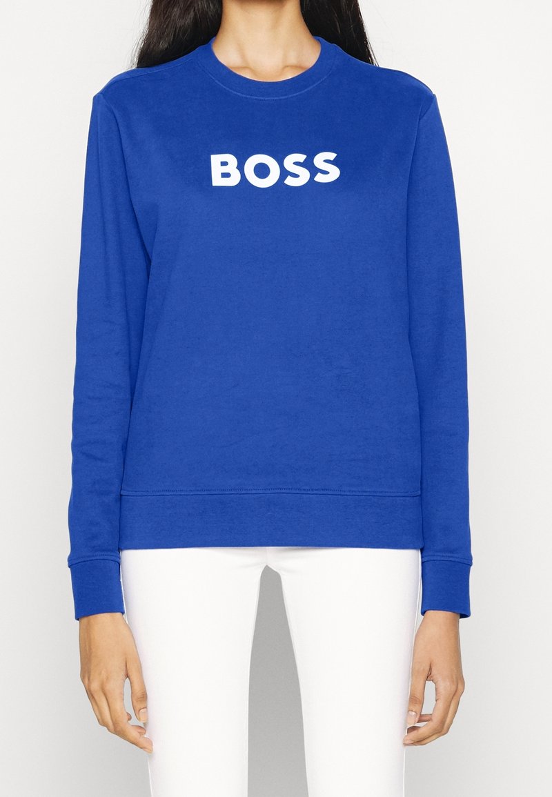 Modrá mikina vyrobená z měkkého materiálu, s kulatým výstřihem a dlouhými rukávy. Na přední straně nápis "BOSS" v tučném bílém písmu.