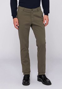 Olivgröna chinos med slim-fit design, utrustade med knäppning, bälteshällor och ett slätt texturerat tyg. Bärs med svarta skor.