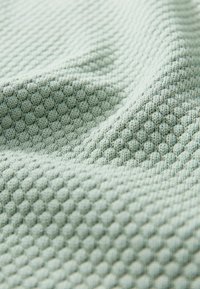 Textured green fabric featuring a honeycomb pattern, showcasing a soft, woven material with subtle depth and varying surface dimension.