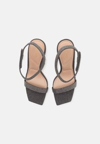 Harmaat kangas korkokengät neliönmuotoisella kärjellä, koristellut hihnat ja pehmeä beige sisäpohja. Varustettu säädettävillä nilkkahihnoilla.