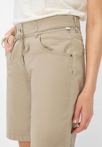 Shorts beige avec une coupe décontractée, taille élastique à cordon, poches latérales, et un tissu lisse et léger. Comprend des détails de couture subtils.