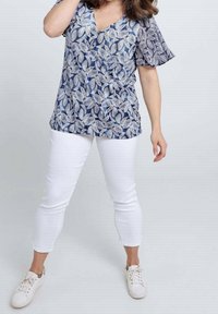 Blauw-wit top met patroon, korte vlindermouwtjes en een V-hals. Gecombineerd met witte slim-fit broek en witte sneakers.