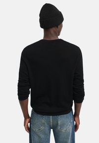 Svart stickad tröja med långa ärmar, rund hals och ribbade mudd, tillsammans med blå denimjeans.