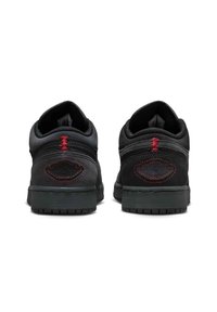 Ζευγάρι μαύρα αθλητικά παπούτσια με κόκκινες ραφές στη φτέρνα και υφή στη μαύρη σόλα, εμφανιζόμενα από πίσω σε λευκό φόντο.